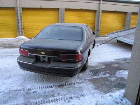1991 Ford LTD Crown Victoria - Rear three-quarter photo of a dark Chevrolet Caprice sedan with a tow strap attached in a snowy storage lot.