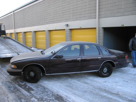 1991 Ford LTD Crown Victoria - Driver-side profile photo of a dark Chevrolet Caprice sedan beside a flatbed tow truck and storage units in the snow.