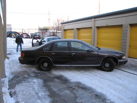 1991 Ford LTD Crown Victoria - Driver-side profile photo of a dark Chevrolet Caprice sedan with a rear door open in a snowy storage lot.