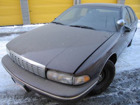 1991 Ford LTD Crown Victoria - Front three-quarter photo of a dusty dark Chevrolet Caprice sedan parked in front of yellow storage doors in the snow.