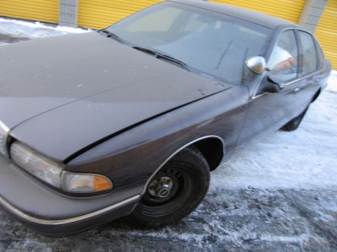 1991 Ford LTD Crown Victoria - Front three-quarter photo of a dusty dark Chevrolet Caprice sedan parked near yellow storage doors in the snow.