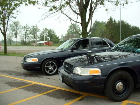 2000 Ford Crown Victoria - Two dark blue Ford Crown Victorias are parked side-by-side in an outdoor lot.