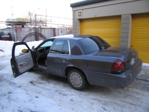 1991 Ford LTD Crown Victoria - Rear three-quarter photo of a gray Ford Crown Victoria sedan with the front door open in a snowy storage lot.