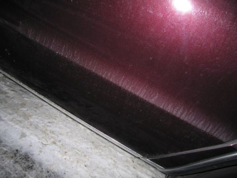 1991 Ford LTD Crown Victoria - Close-up photo of a maroon car body panel and chrome rocker trim showing surface texture.
