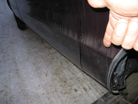 1991 Ford LTD Crown Victoria - Close-up photo of a hand pulling rubber bumper trim away from a dark car rocker and quarter panel.