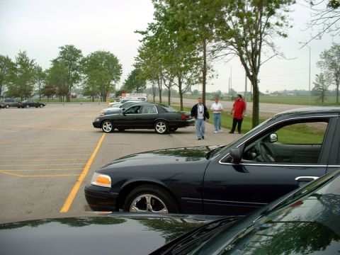 2000 Ford Crown Victoria - A dark blue 2000 Ford Crown Victoria is parked in a lot with other vehicles and people nearby.