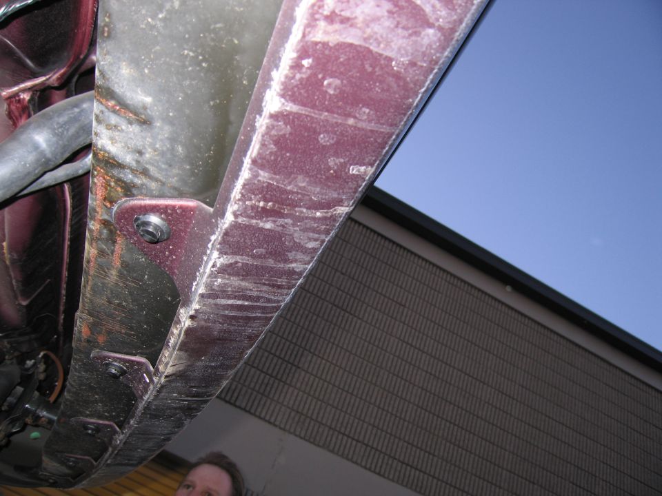Upward photo of a vehicle underbody panel against blue sky and a building