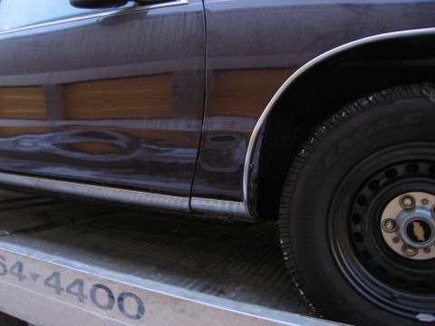 1991 Ford LTD Crown Victoria - Photograph of a car's woodgrain side and wheel on a flatbed, not a technical document.