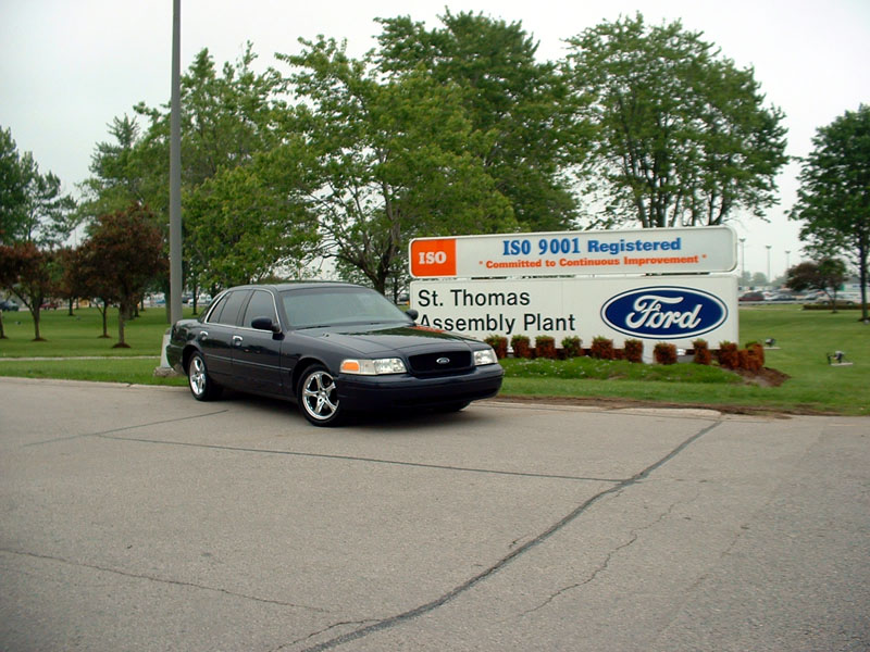 Lowered dark blue Crown Victoria beside the St. Thomas Assembly Plant Ford sign