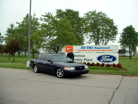 2000 Ford Crown Victoria - A dark blue 2000 Ford Crown Victoria is parked in front of the Ford assembly plant sign.