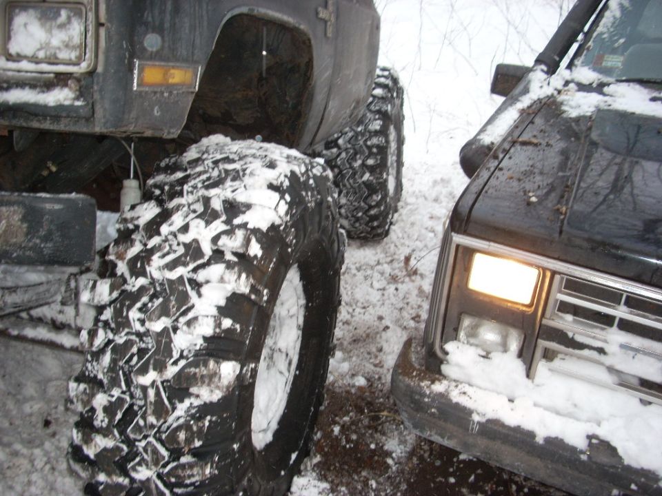 Two off-road vehicles in snow, one with headlight on.