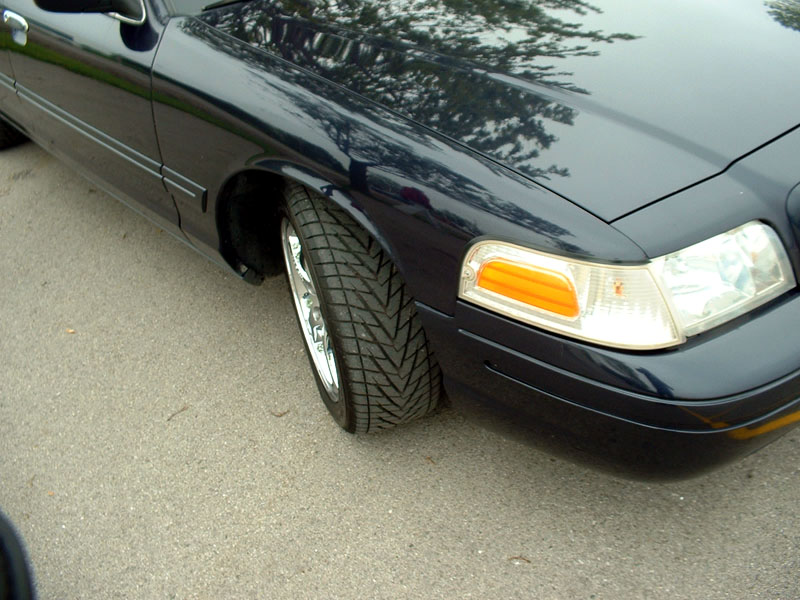 Front corner of a dark blue Crown Victoria with polished wheel and wide tire