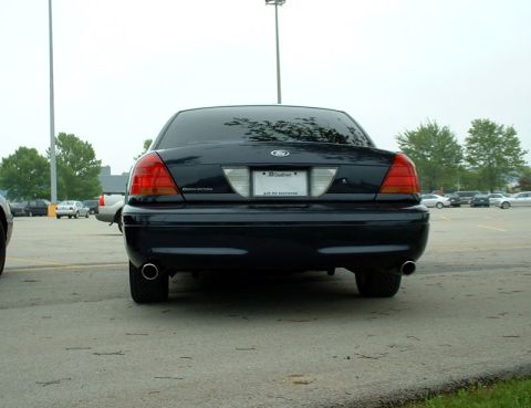 2000 Ford Crown Victoria - Rear view of a 2000 Ford Crown Victoria parked in a lot with other vehicles and trees in the background.