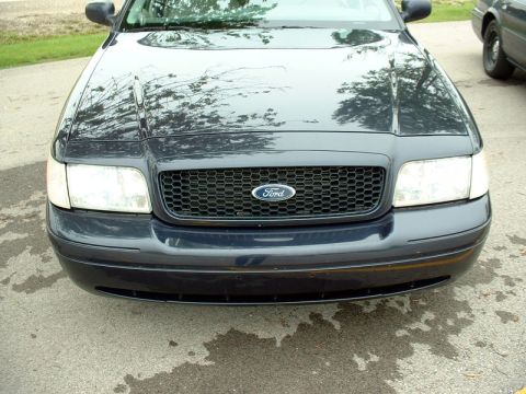 2000 Ford Crown Victoria - The front grille and headlights of a dark blue Ford Crown Victoria are shown, with a portion of another vehicle visible to the right.