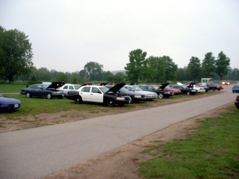 2000 Ford Crown Victoria - A fleet of Ford Crown Victoria police cars are parked in a row with their hoods open.