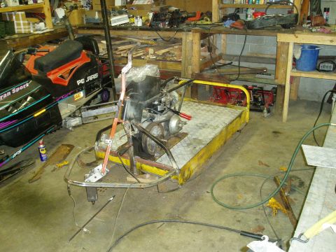 2000 Ford E350 - A disassembled engine sits on a yellow utility cart next to a Polaris snowmobile in a cluttered garage or workshop setting. Various tools a…