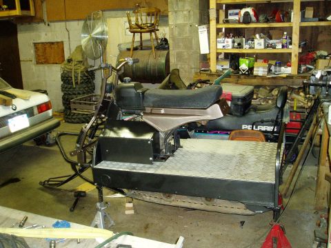2000 Ford E350 - A custom-built tracked vehicle with a motorcycle-like front end and a cargo bed is supported by jack stands in a garage. A white car is par…