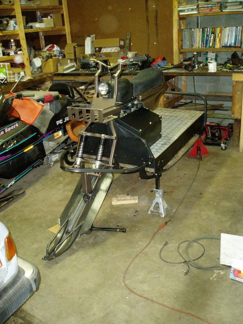 2000 Ford E350 - A custom-built, multi-passenger snowmobile is parked in a cluttered garage. The snowmobile features a long, flat cargo bed with a diamond p…