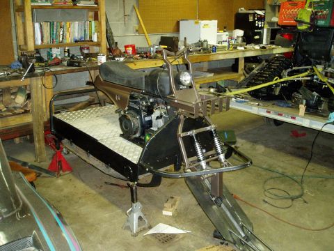2000 Ford E350 - A custom-built, single-person snowmobile is shown in a workshop setting, supported by jack stands. The vehicle features a small engine, a s…