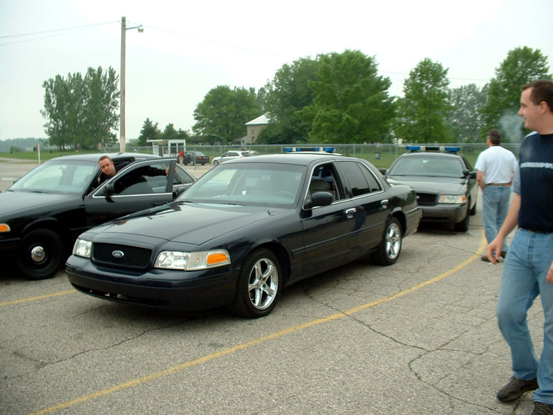 Dark blue Ford Crown Victoria on polished wheels parked among police Crown Vics