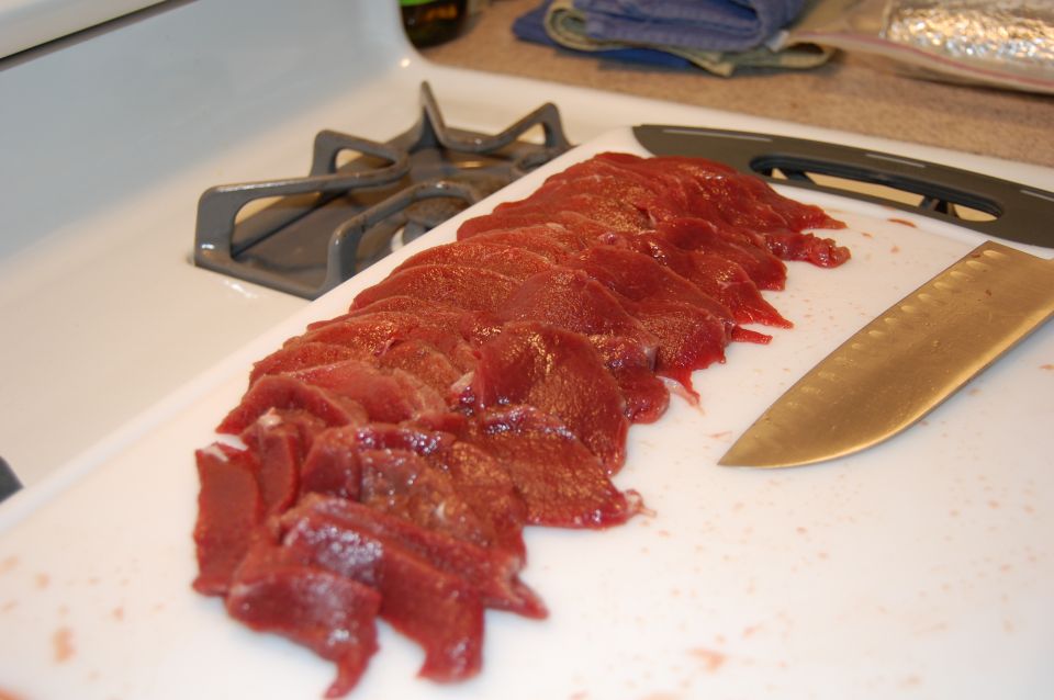 Sliced raw meat on a cutting board with a knife