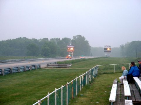 2000 Ford Crown Victoria - Two cars race down a drag strip under a hazy sky, with spectators watching from the side.