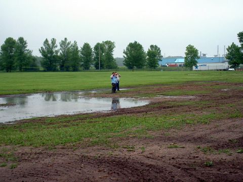 2000 Ford Crown Victoria - A muddy field with puddles and a few people standing near the water, with industrial buildings in the background.