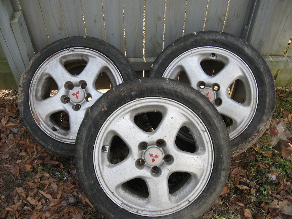 Three silver alloy wheels with tires and Mitsubishi logos, on the ground.