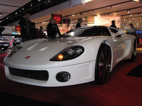 1996 Ford Probe - A white custom sports car with red accents is displayed on a red carpet at an auto show. The car features a prominent front grille, large h…