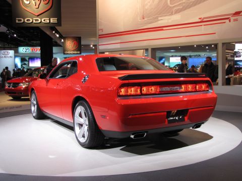 1996 Ford Probe - The rear view of a bright red Dodge Challenger SRT8 is displayed on a white circular platform in what appears to be an auto show. The car f…