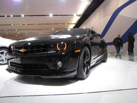 1996 Ford Probe - A black Chevrolet Camaro is displayed on a white platform with people in the background.