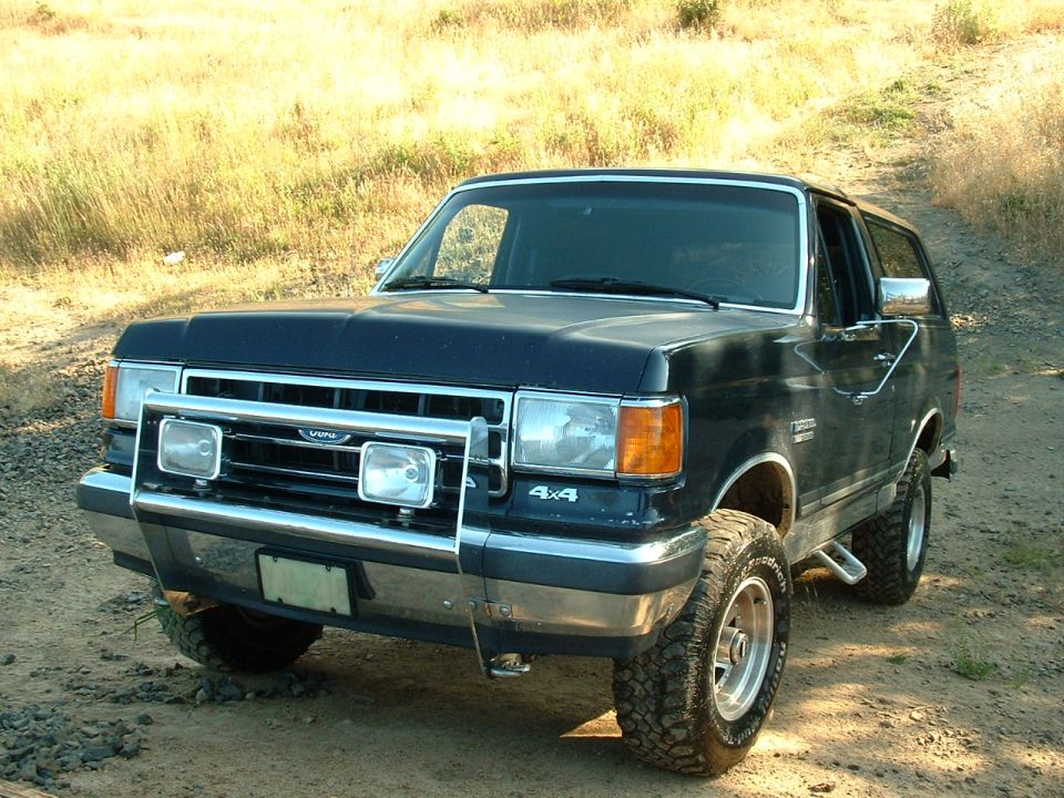 Dark blue Ford Bronco 4x4 with chrome brush guard and driving lights on a dirt track