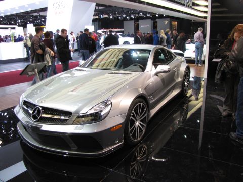 1996 Ford Probe - A silver Mercedes-Benz SL-Class roadster is displayed on a black reflective surface at an auto show. The car features a prominent Mercedes-…