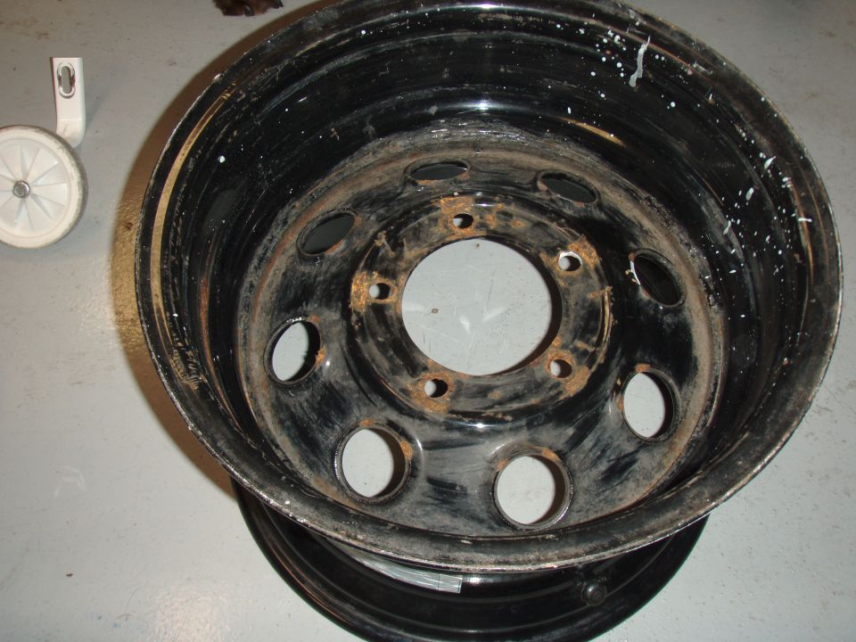 Rusty black steel wheel rim with white paint splatters, and a small white wheel.