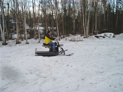 2000 Ford E350 - A person in a yellow jacket and blue jeans rides a vintage snowmobile through a snowy, wooded area. The snowmobile has a black seat and a m…