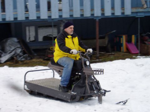 2000 Ford E350 - A man wearing a yellow jacket and blue jeans rides a homemade snowmobile through the snow. The snowmobile has a flat cargo bed at the rear…