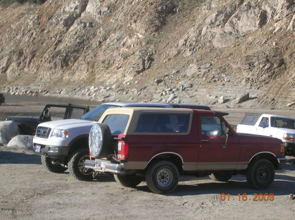 Maroon Ford Bronco with tan top parked next to a white Ford F-150 pickup truck.