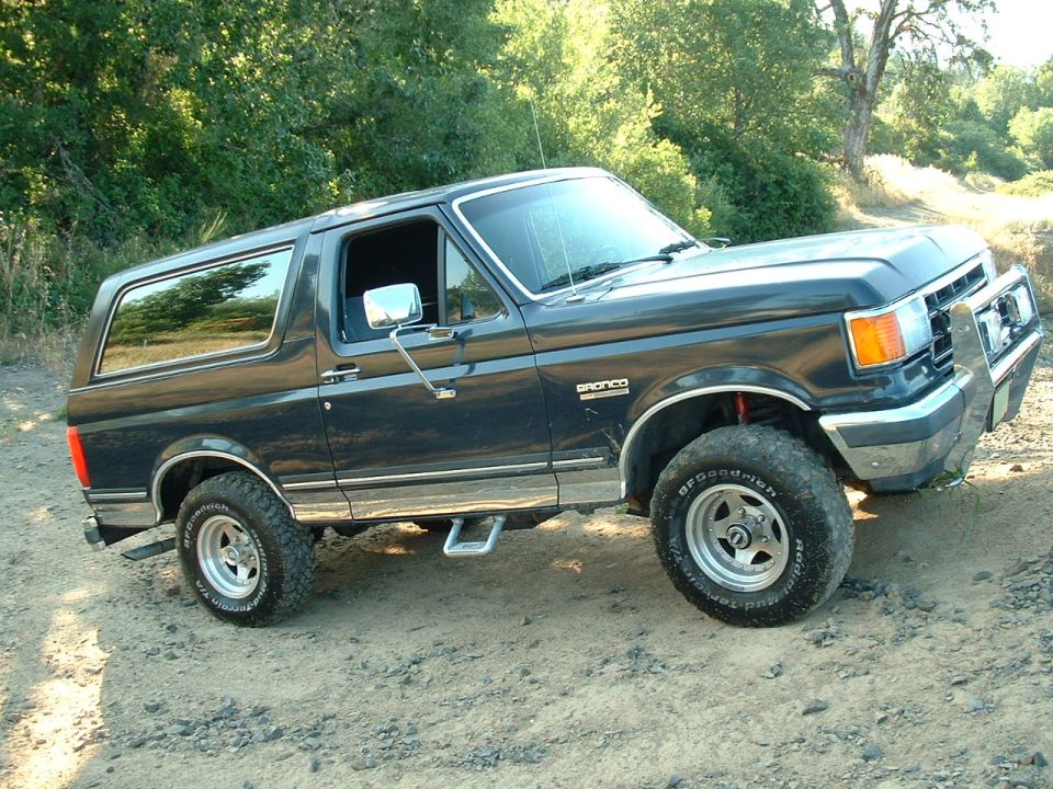 Dark blue lifted two-door Ford Bronco SUV, passenger side, on dirt trail