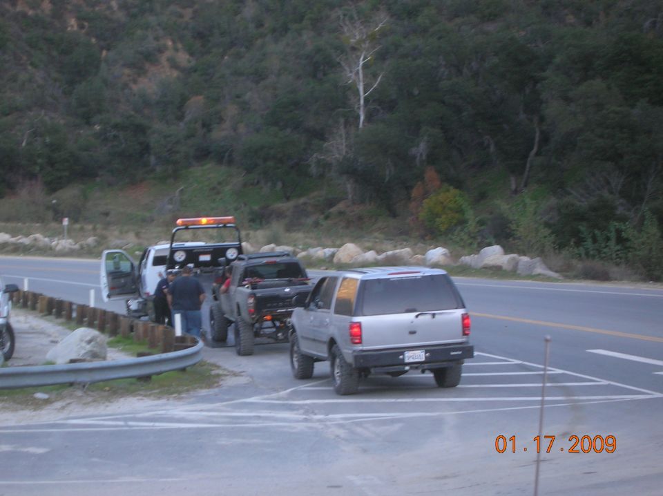 Tow truck with a lifted pickup and a silver SUV on the side of a road.