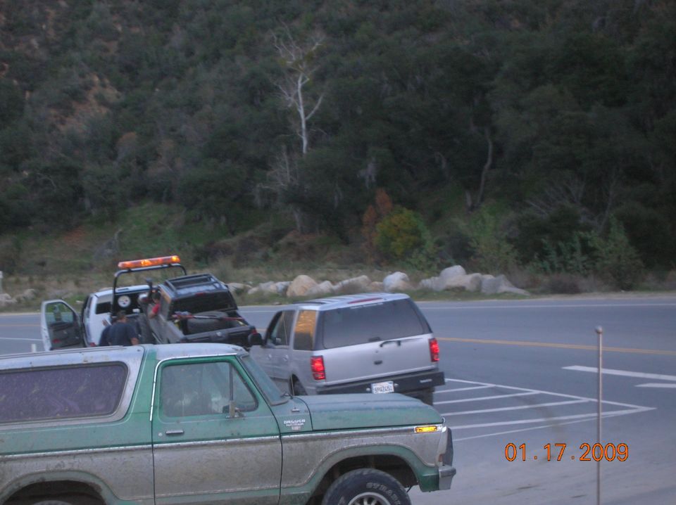 Tow truck loading SUV, with a classic Ford Bronco in the foreground.
