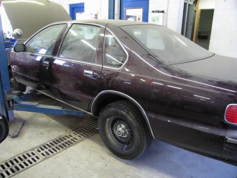 1991 Ford LTD Crown Victoria - A dark-colored sedan is raised on a lift inside a garage, with its hood open.