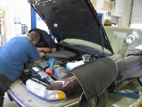 1991 Ford LTD Crown Victoria - Two mechanics work on the engine of a dark sedan with its hood open.