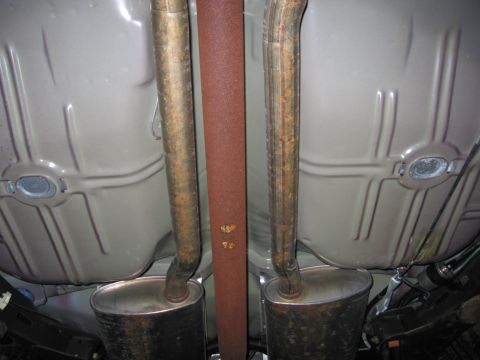 1991 Ford LTD Crown Victoria - The underside of a vehicle reveals its dual exhaust system and driveshaft, with visible signs of rust on the exhaust components.