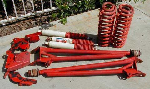 1991 Ford Bronco - A collection of red-painted suspension components laid out on a concrete driveway, including two coil springs, several Rancho shock absorbe…