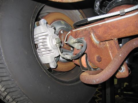 1991 Ford LTD Crown Victoria - Detail of a vehicle's rear brake assembly and suspension, showing significant rust on the metal components.