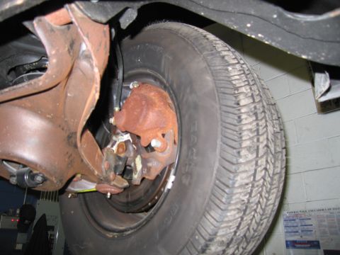 1991 Ford LTD Crown Victoria - A close-up view of a vehicle's undercarriage reveals a tire and heavily rusted suspension parts.