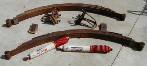 1991 Ford Bronco - Two rusty multi-leaf springs laid on a concrete surface along with U-bolts, mounting brackets, and two red-and-white Rancho shock absorbers…