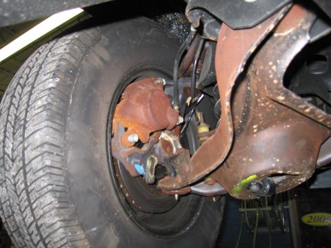 1991 Ford LTD Crown Victoria - Close-up view of the front wheel brake assembly, showing a rusty caliper and tire.