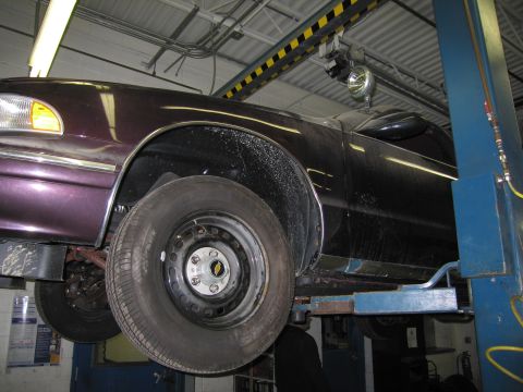1991 Ford LTD Crown Victoria - A dark purple sedan is raised on a car lift in a garage, showing its front wheel and fender.