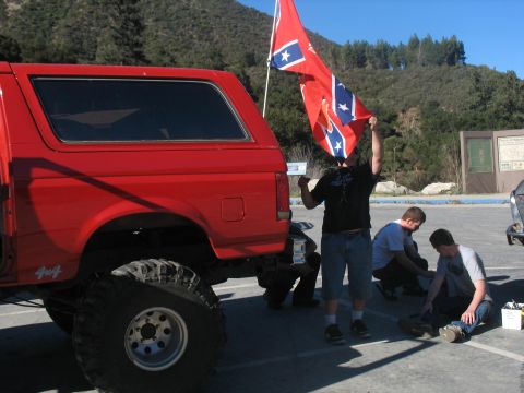 1987 Ford Bronco - A red 1987 Ford Bronco is parked outdoors with several people nearby, one holding a flag.
